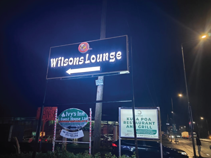 Illuminated Wilsons Lounge directional lightbox sign in Nairobi Kenya showing left arrow for restaurant entrance at night