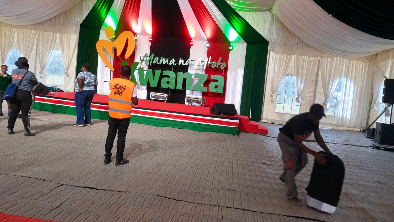 Crew installing Mama na Mtoto Kwanza letters on a draped event stage.
