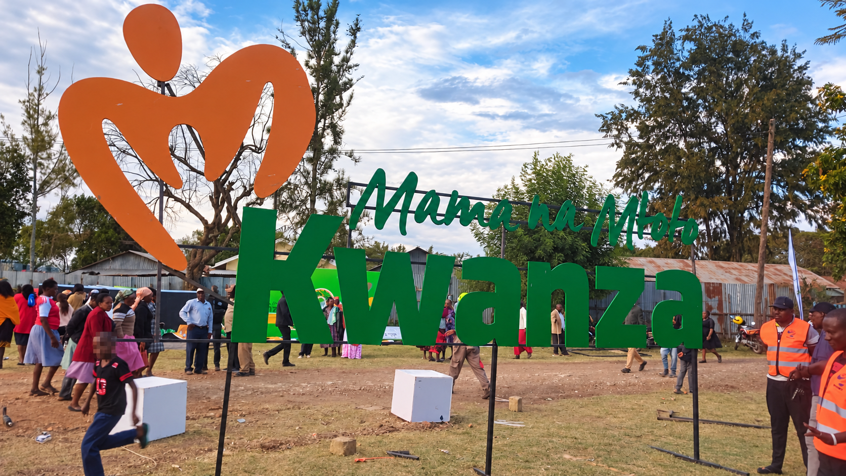 Large green Mama na Mtoto Kwanza entrance letters and orange logo outdoors.