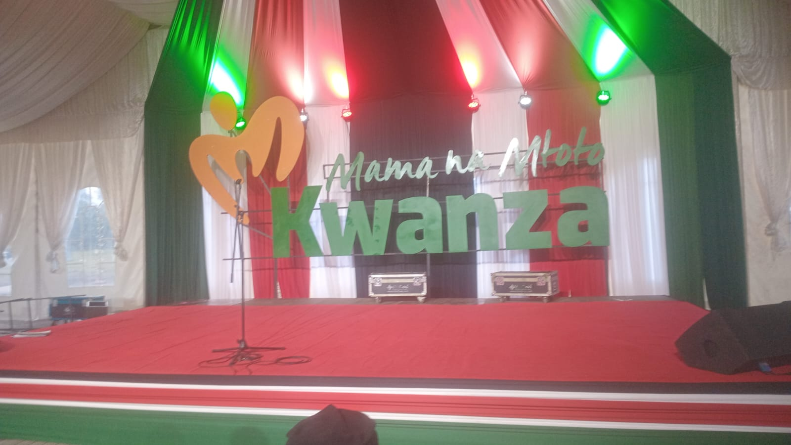 Mama na Mtoto Kwanza stage lettering with red, white, black and green draping.