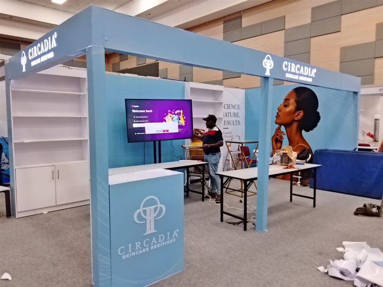 Light blue Circadia exhibition booth with illuminated branding, shelving and a front counter during setup.